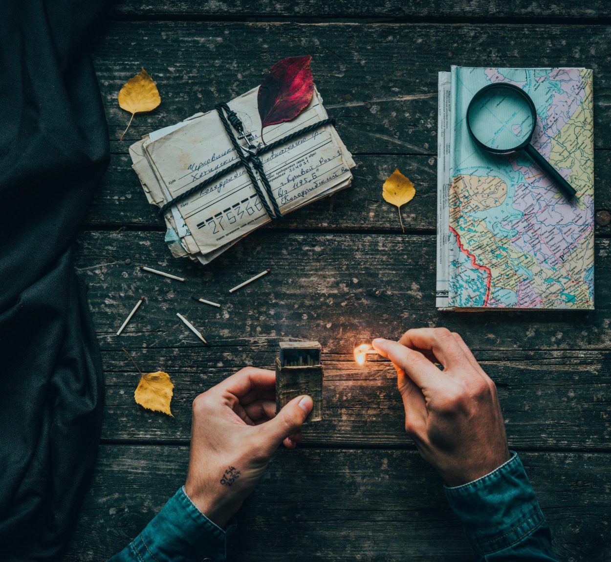 A creative flat lay featuring a map, letters, and a match being ignited on a vintage wooden table.
